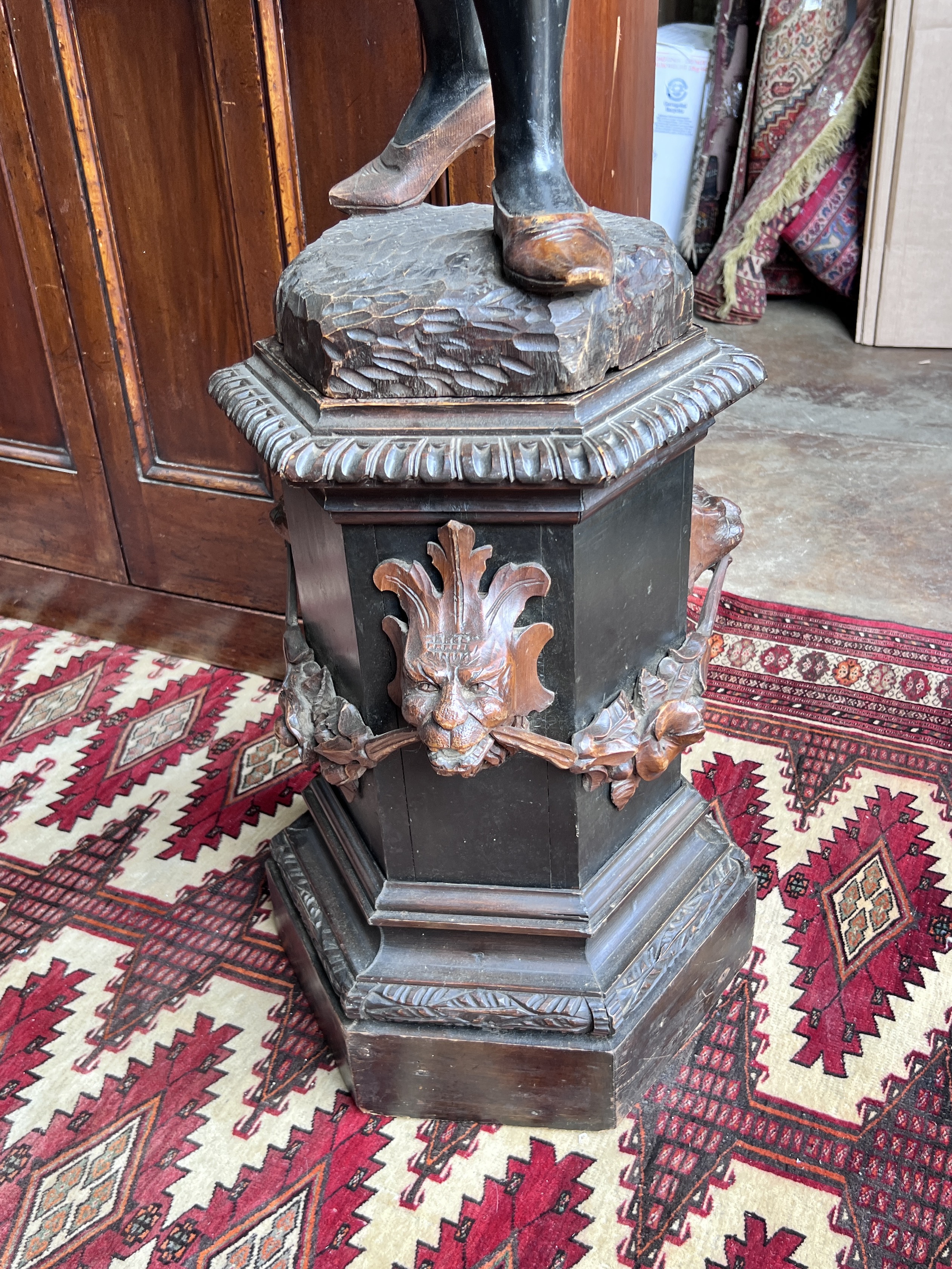 An early 20th century carved wood Blackamoor on associated hexagonal lion mask swagged plinth, height 193cm